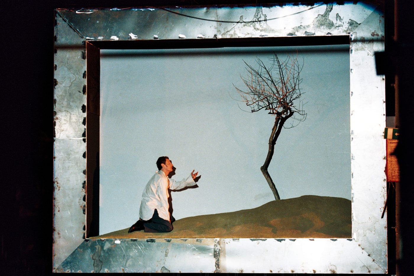 Graal - uomo in preghiera davanti a un albero spoglio dentro una cornice metallica, regia Corsetti, scene Taraborrelli, Officine Molliconi Roma 2000