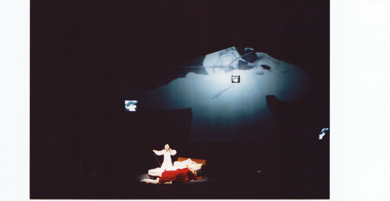 La Voix Humaine - grande proiezione video di un volto femminile e piccola figura in scena con letto rosso, Opera Roma 2001, scenografia Taraborrelli/Corsetti